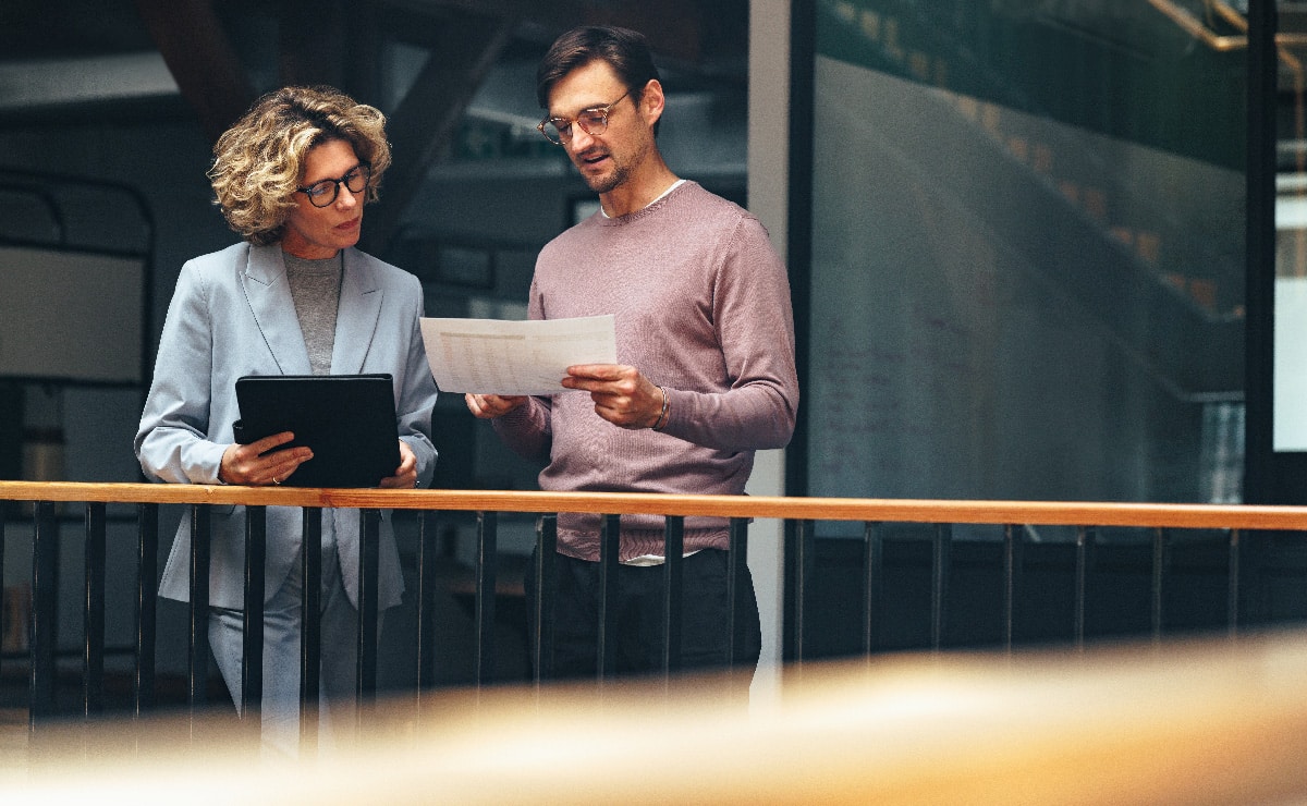 Ein Mann und eine Frau in geschäftlicher Kleidung stehen zusammen und besprechen Finanzdokumente.